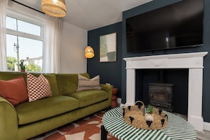 Ein Wohnzimmer mit einem grünen Sofa, einem Kamin, einem Fernseher und einem Tisch mit Muster.
