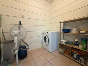 Une buanderie équipée d’un lave-linge, d’un ventilateur et d’étagères contenant des produits de nettoyage.