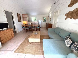 A cozy living room with a sofa, a coffee table, and a TV. There's a kitchen area with a fridge and a dining table. - Maison climatisée dans domaine avec piscine à Gassin (GASSIN)