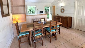 Un coin repas avec une table et des chaises en bois, un espace cuisine doté de placards et une fenêtre donnant sur un espace verdoyant.