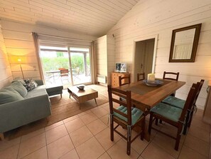 A living room with a sofa, a coffee table, a dining table with chairs, a television, and a sliding glass door leading to a patio. - Maison climatisée dans domaine avec piscine à Gassin (GASSIN)