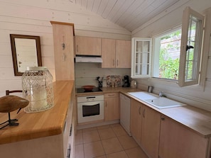 A compact kitchen with wooden cabinets, a built-in oven, a sink, and a window with a view of greenery outside. - Maison climatisée dans domaine avec piscine à Gassin (GASSIN)