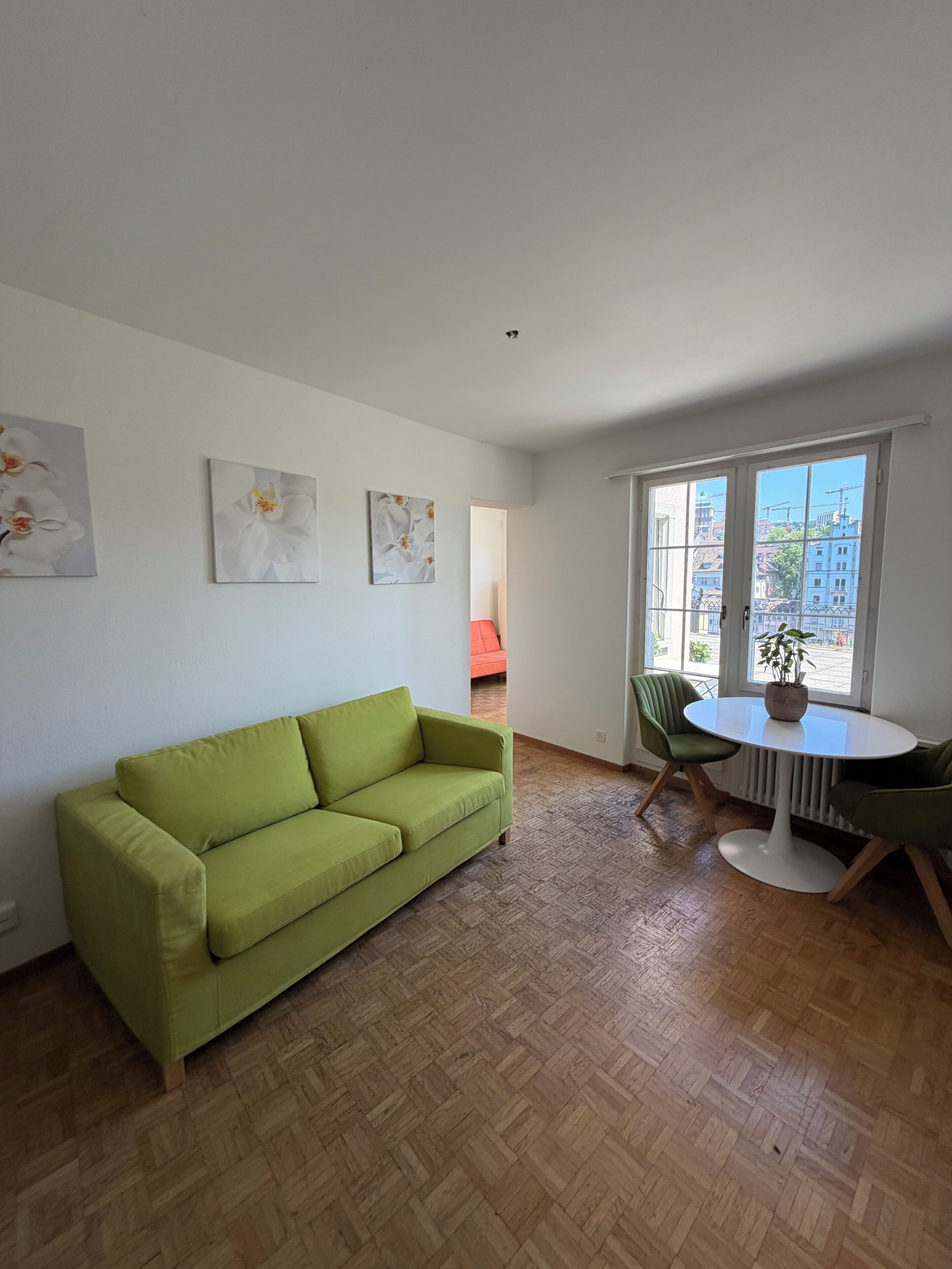 Una habitació amb un sofà verd, una taula rodona amb cadirees i obres d'art a les parets.