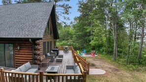 Une cabane en rondins avec une terrasse, du mobilier d’extérieur et une vue sur la forêt.