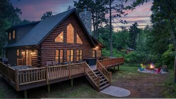 Una cabaña de troncos con un balcón, chimenea y una escalera que lleva a la entrada principal.