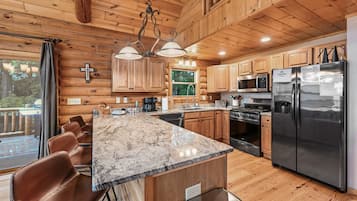 Cocina de cabaña de madera con una isla de mármol, armarios de madera, electrodomésticos de acero inoxidable y un comedor con sillas de cuero.
