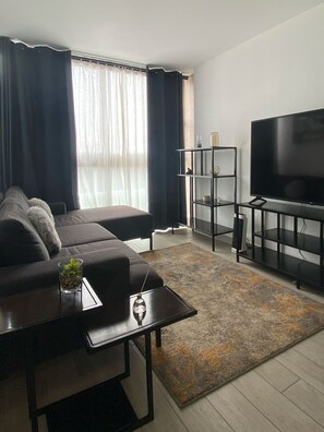 A modern living room with a sofa, a coffee table, a TV on a stand, and a bookshelf. - Barranco Bohemio | Modern Apartment located in the most vibrant part of Lima. (Barranco)