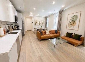A modern living room with a sofa, a glass coffee table, and a kitchen area with cabinets and a sink. - High-End Center City 2 Bed & 2 Bath Apartment (Philadelphia)
