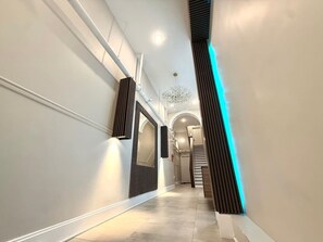Un couloir moderne avec un escalier, un luminaire décoratif et un mur d’accent bleu.