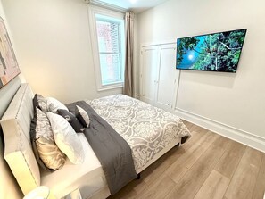 Une chambre à coucher avec un lit, une télévision, une fenêtre avec des rideaux et une porte.