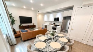 A modern kitchen with white cabinets, a stainless steel refrigerator, and a dining area with a marble table and chairs.