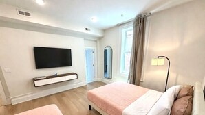 A hotel room with a bed, a TV mounted on the wall, and a window with curtains.