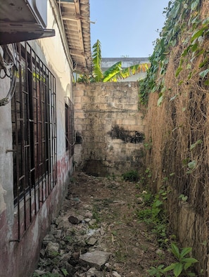 A narrow alleyway with a stone wall, a metal gate, and overgrown vegetation. - Charming 2-bedroom Apartment in Punta Hansa, San Andrés (San Andrés)