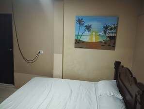A bedroom with a bed, a painting of a beach scene, and a power outlet on the wall. - Charming 2-bedroom Apartment in Punta Hansa, San Andrés (San Andrés)