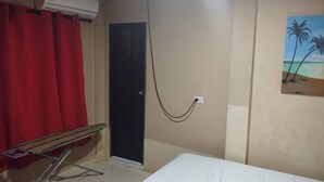 A room with a bed, a red curtain, a door, an air conditioning unit, and a painting of palm trees.