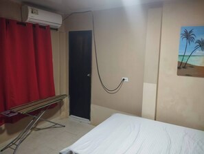 A room with a bed, a red curtain, a door, an air conditioning unit, and a painting of palm trees.