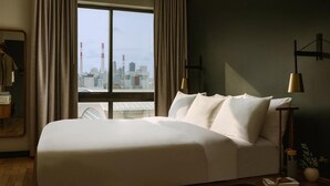 Ett modernt hotellrum med en stor säng, utsikt över staden och en minimalistisk inredning.