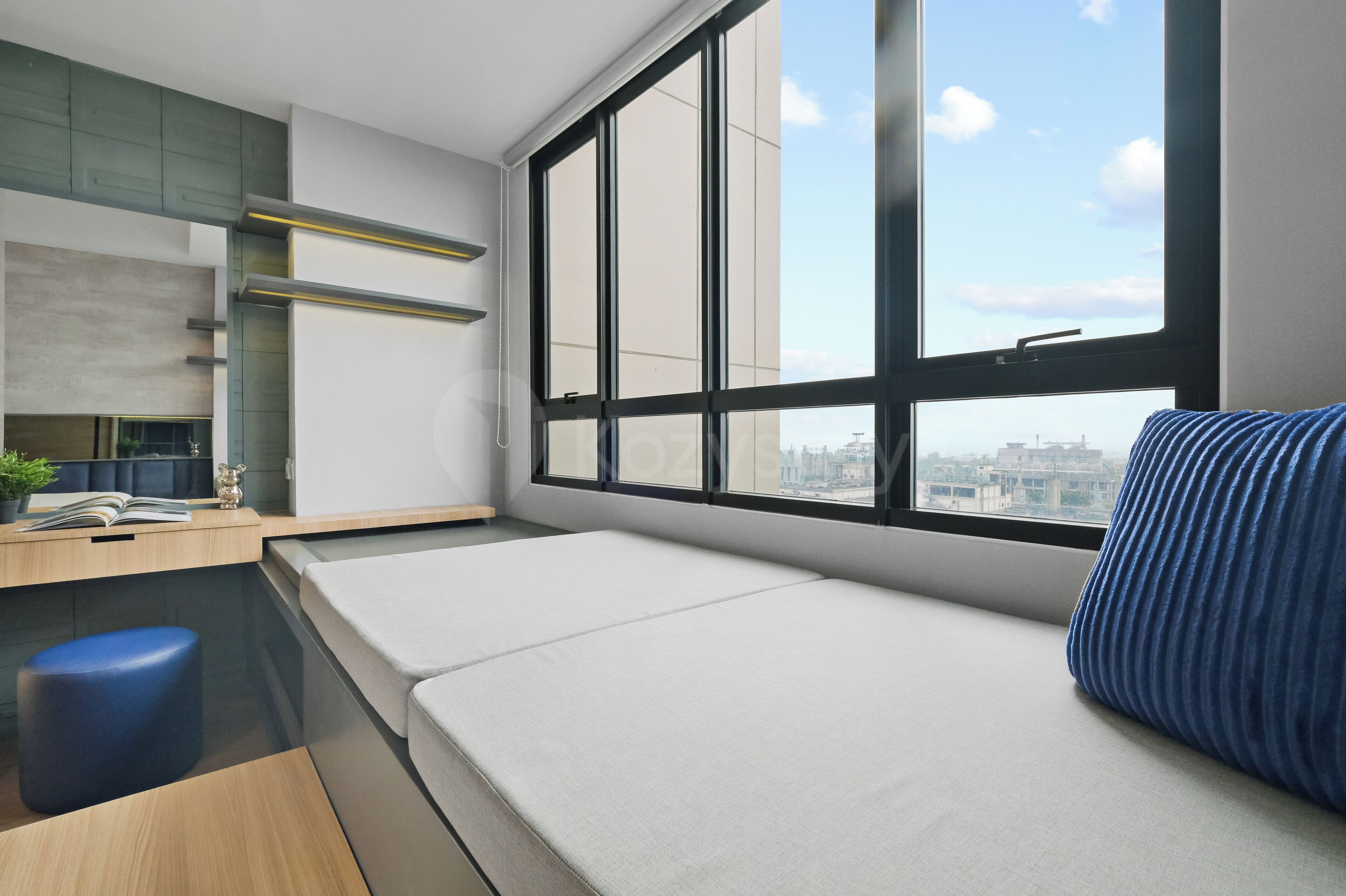 Habitació moderna amb llit, escriptori, tamboret blau i finestra gran amb vista a la ciutat.