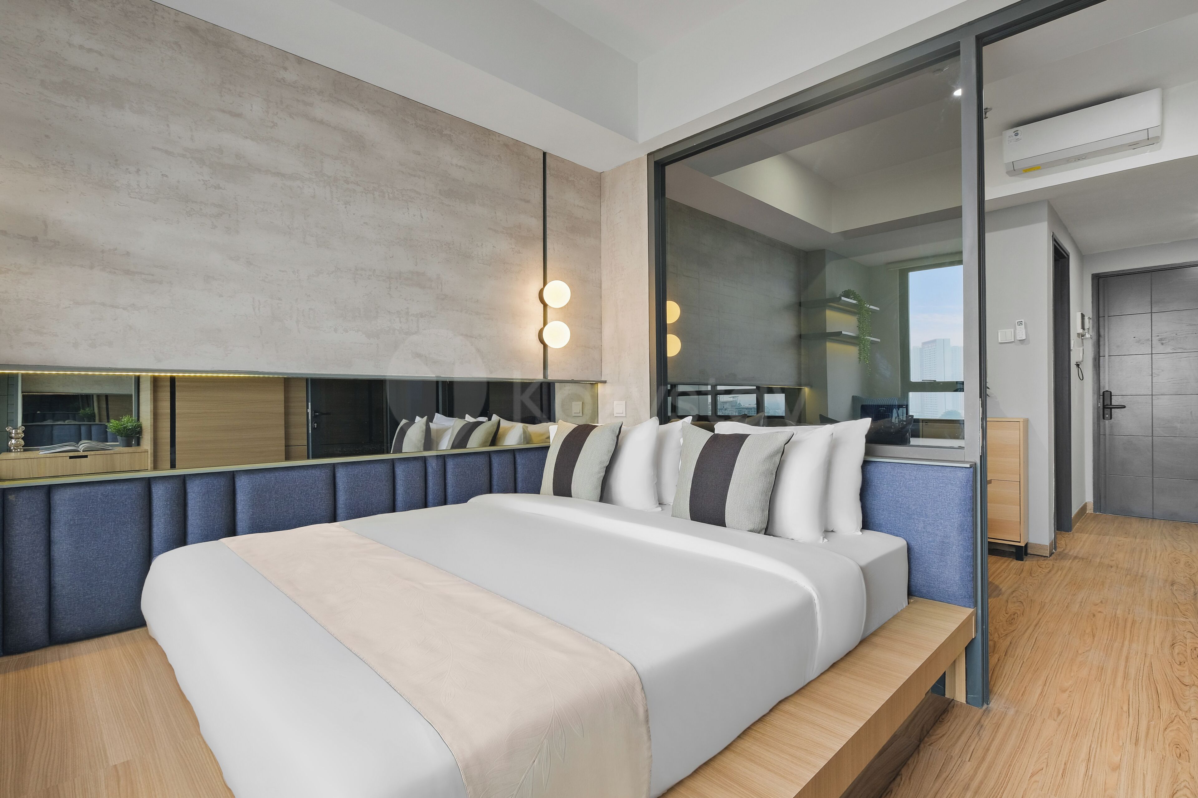 A modern bedroom with a large bed, a built-in bench, a glass wall, and a city view.