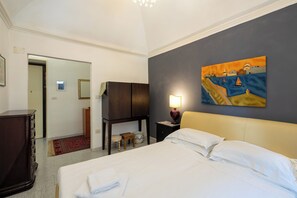 A hotel room with a bed, a nightstand with a lamp, a painting on the wall, and a view of the hallway. - La Casetta di Piazza Vittorio (Rome)