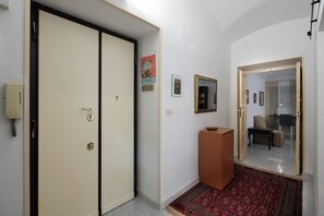 A hallway with a double door, a small wooden cabinet, a framed artwork, and a mirror reflecting a room with a desk and chair. - La Casetta di Piazza Vittorio (Rome)