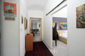 A hallway leading to a bedroom with a bed, a desk, and chairs. There are paintings on the walls and a carpeted floor. - La Casetta di Piazza Vittorio (Rome)