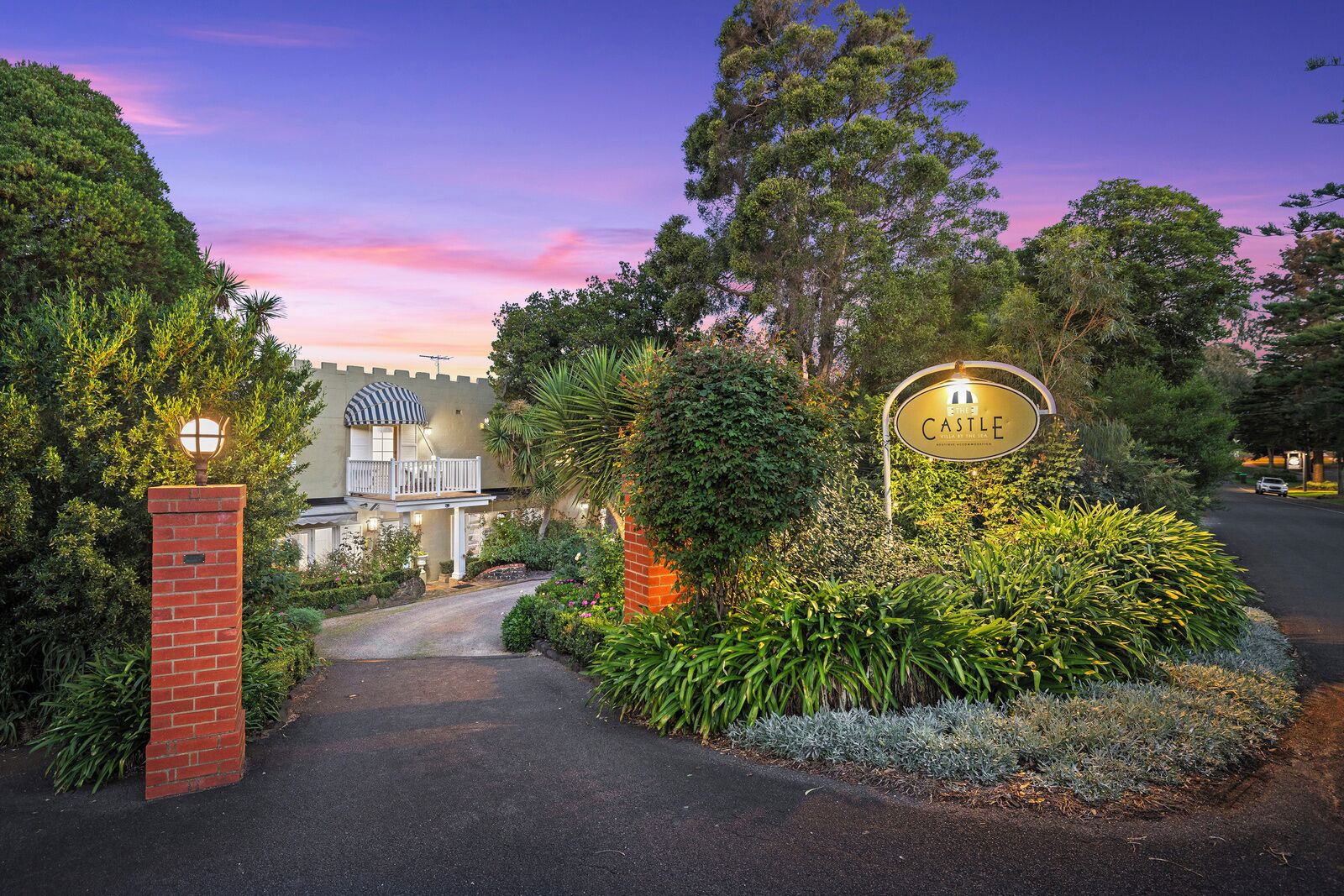 A gated entrance with a sign reading 'The Castle Hotel,' surrounded by lush greenery and a pathway leading to the building.