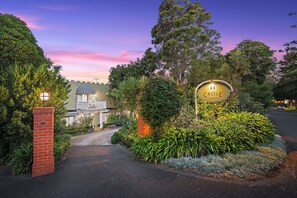 A gated entrance with a sign reading 'The Castle Hotel,' surrounded by lush greenery and a pathway leading to the building.