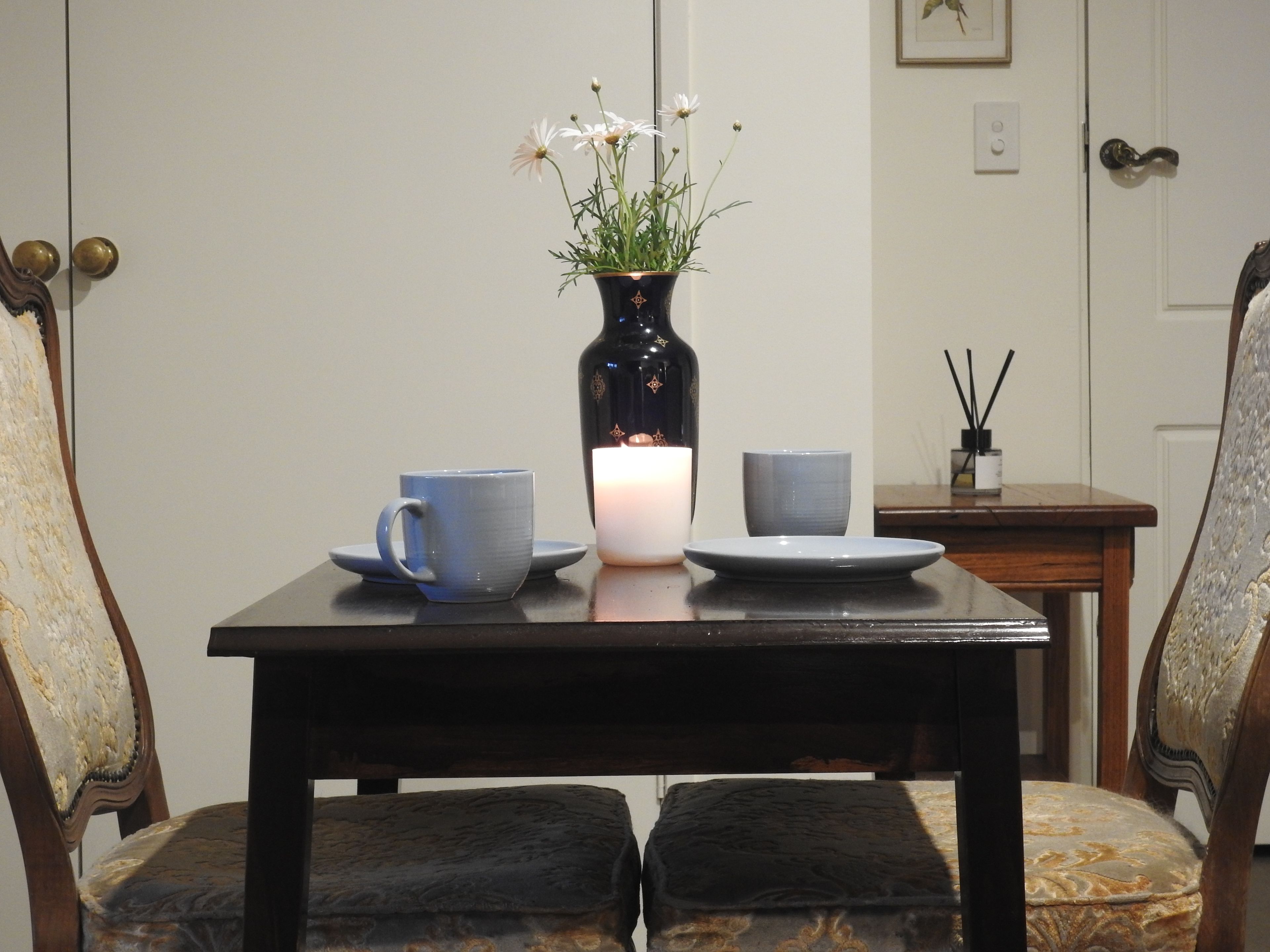 A dining table with a vase of flowers, two cups, and a candle.