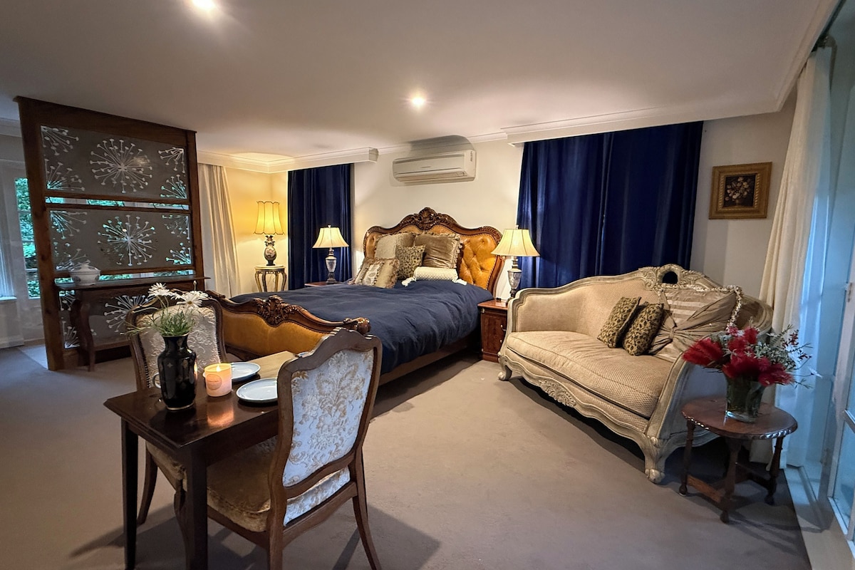 A bedroom with a bed, a sofa, a table with a vase, and a window with curtains.