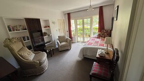 A room with a sofa, armchair, and a bed with a red and white checkered bedspread. There is a television on a stand, a small table, and a chair with a plaid cushion. - The Castle - Villa by the Sea (Cowes)