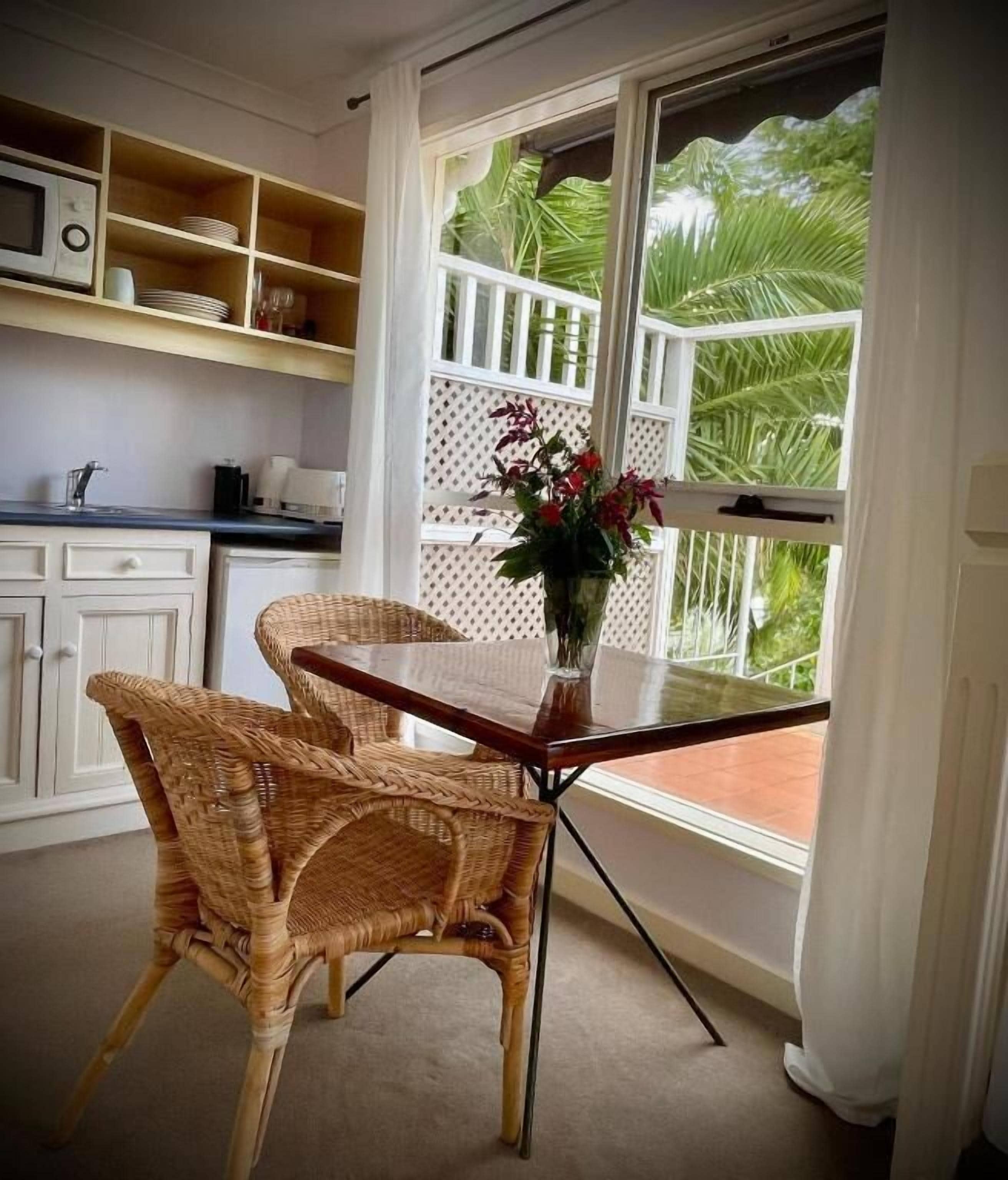 A kitchen with wicker chairs, a dining table, and a window with a view of greenery.