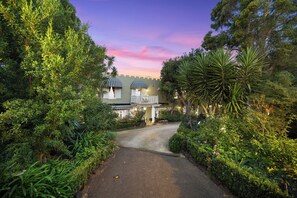 A pathway leading to a building with a balcony, surrounded by lush greenery.