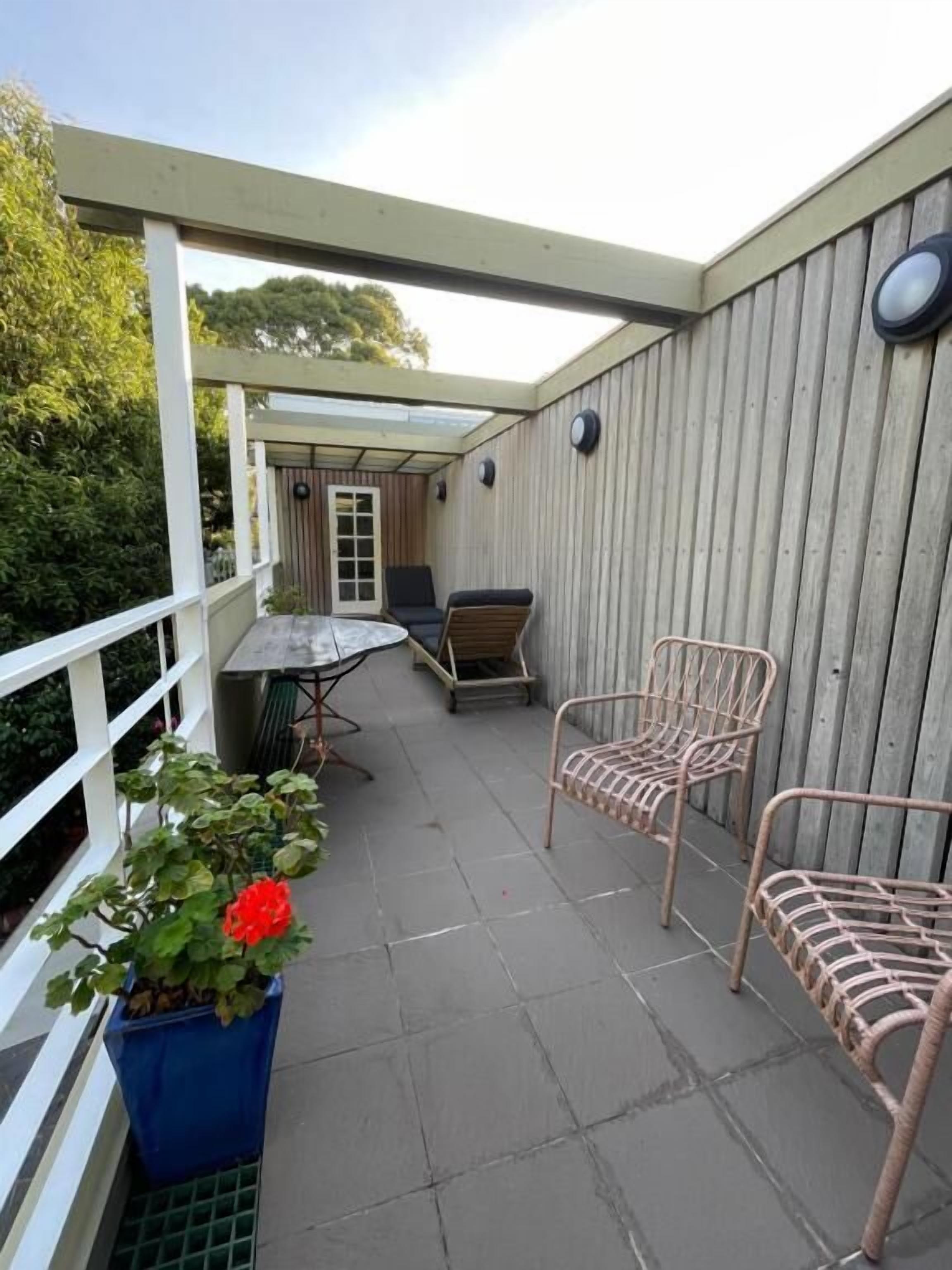 A covered patio area with a table and two chairs, a potted plant, and a wooden wall.
