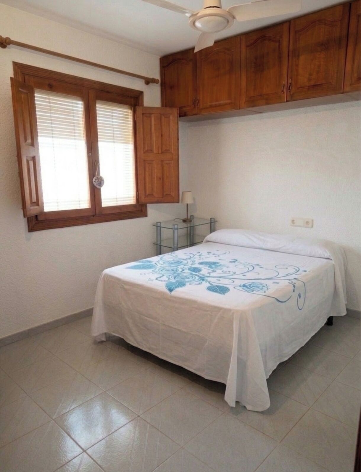 A bedroom with a bed, wooden cabinets, a ceiling fan, and a window with blinds.