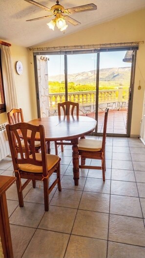 A dining area with a round table and wooden chairs, a ceiling fan, and a view of a mountainous landscape through large glass doors. - Villa Luna: A cozy and peaceful villa with a pool and views, just 15 minutes from the beach (Montesano)