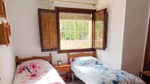 Un dormitorio con dos camas individuales, una mesita de noche de madera, una pequeña mesa y un ventilador de techo.