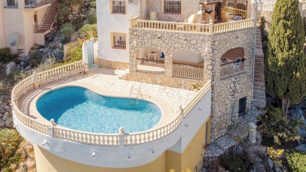 Una casa de varios pisos con piscina, muros de piedra y un balcón.