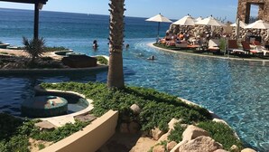 Zona de piscina amb gandules i paraigües, una palmera i vista al mar.