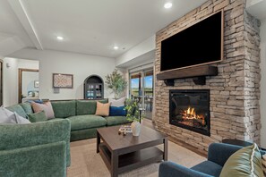 Ein Wohnzimmer mit Kamin aus Stein, einem grünen Sofa und einem an der Wand montierten Flachbildfernseher.