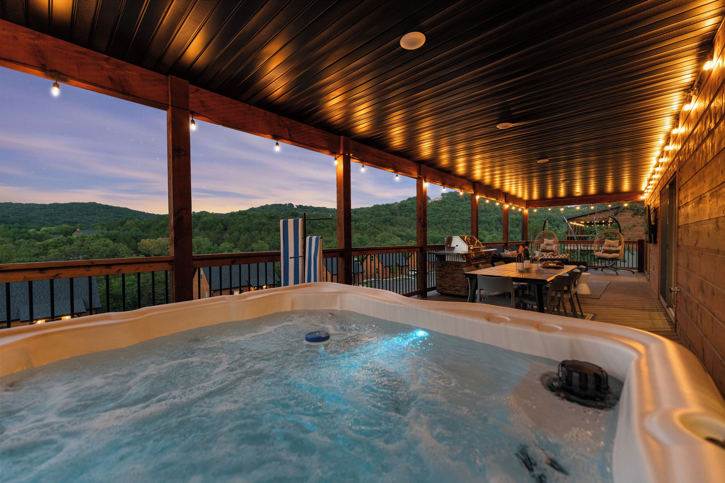 A hot tub with a wooden deck, outdoor furniture, and a view of the hills.