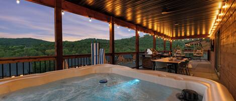 A hot tub with a wooden deck, outdoor furniture, and a view of the hills.