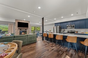 A modern kitchen with dark blue cabinets, a stainless steel refrigerator, and a flat-screen TV mounted above the counter. - New 6BR Cabin with Hot Tub, Fire Pit, Indoor Pool - Game Table, Shuffleboard (Hollister)
