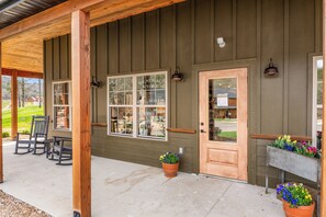 A building with a porch, wooden pillars, a door, and windows. - New 6BR Cabin with Hot Tub, Fire Pit, Indoor Pool - Game Table, Shuffleboard (Hollister)