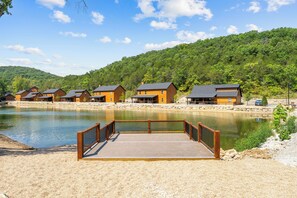 A lakeside property with wooden cabins, a dock, and a forested hillside. - New 6BR Cabin with Hot Tub, Fire Pit, Indoor Pool - Game Table, Shuffleboard (Hollister)