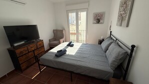 Una camera da letto con un letto, una televisione, una sedia, un comodino e una finestra.