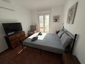 Ein Schlafzimmer mit Bett, Fernseher, Stuhl, Nachttisch und Fenster.