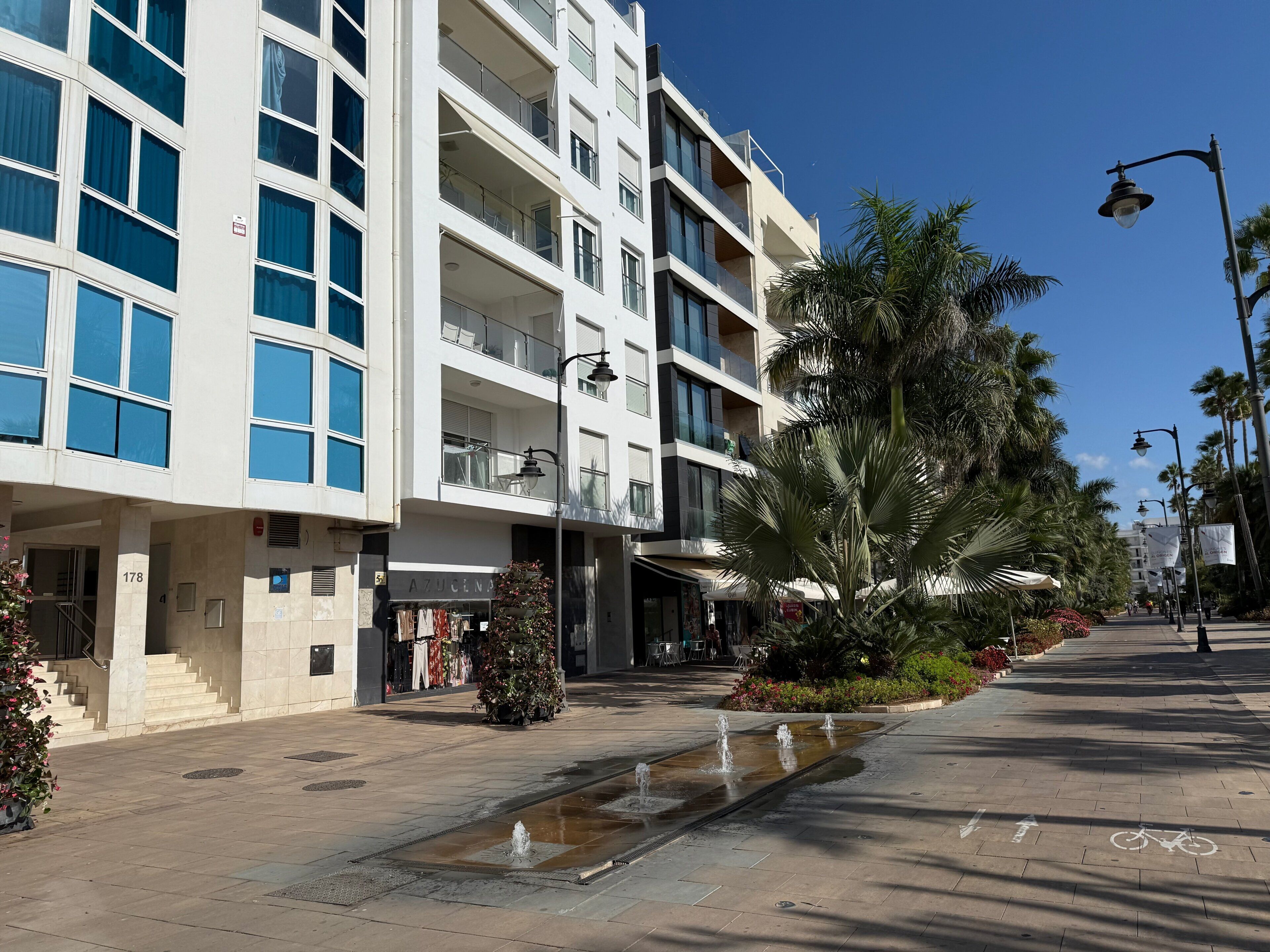 A multi-story building with balconies, a water feature, and a bike lane.