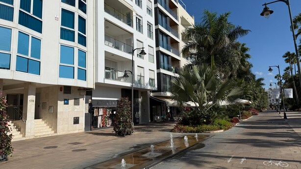 Un edificio a più piani con balconi, un'area con giochi d'acqua e una pista ciclabile.