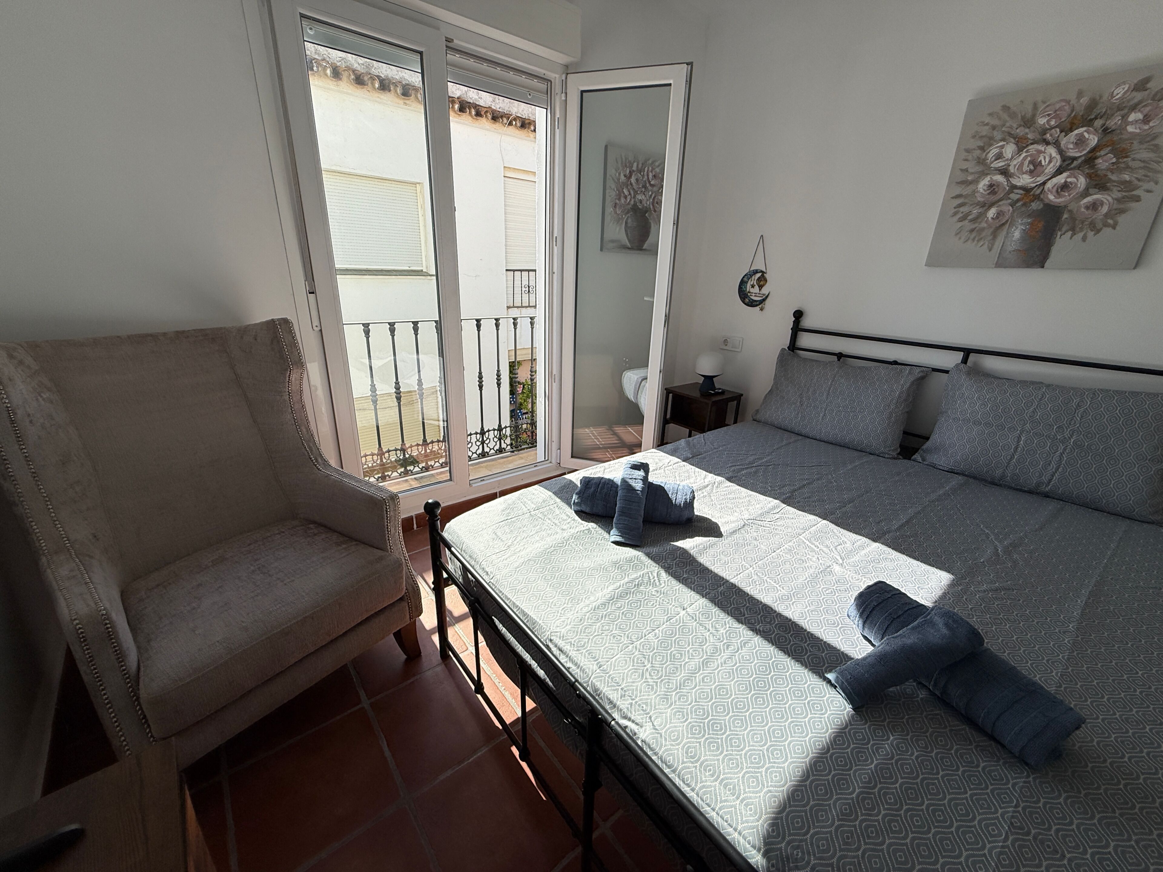 A bedroom with a bed, a chair, a nightstand, and a painting on the wall.